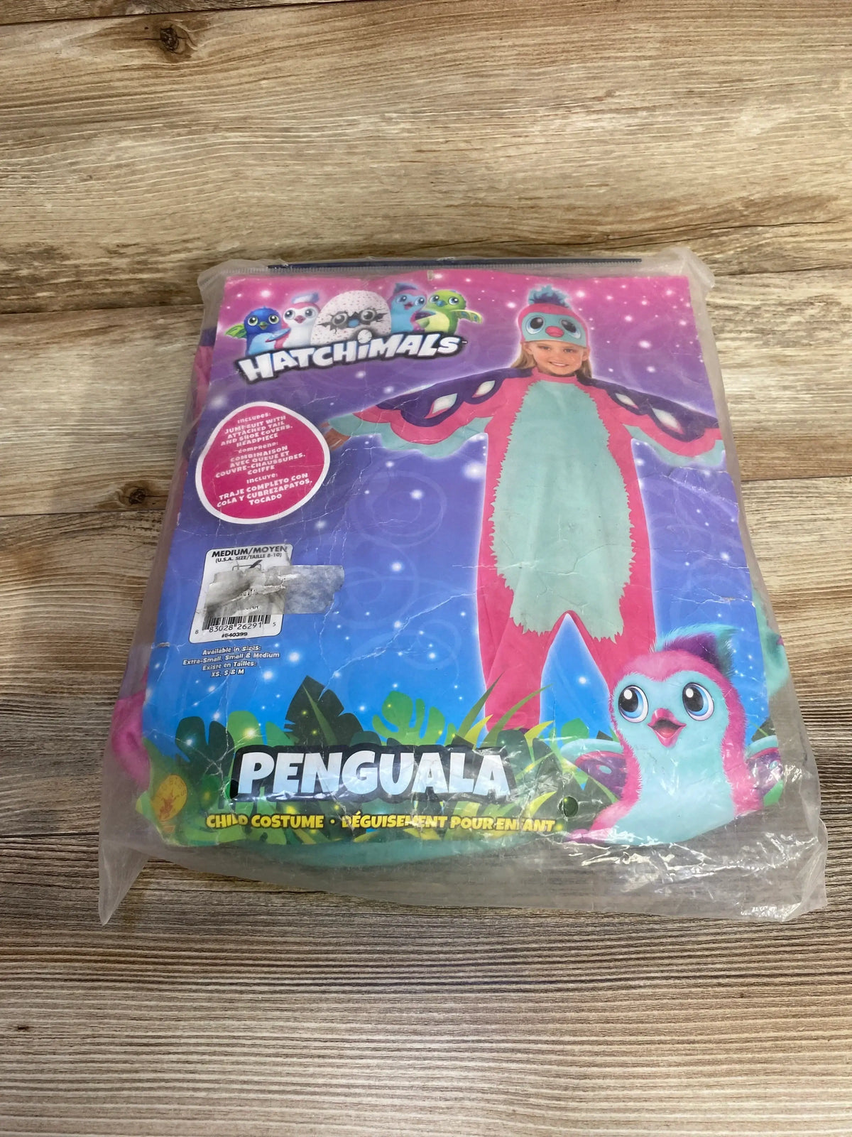 Front view of pink Hatchimals Penguala costume package in clear plastic on a wood-grain surface