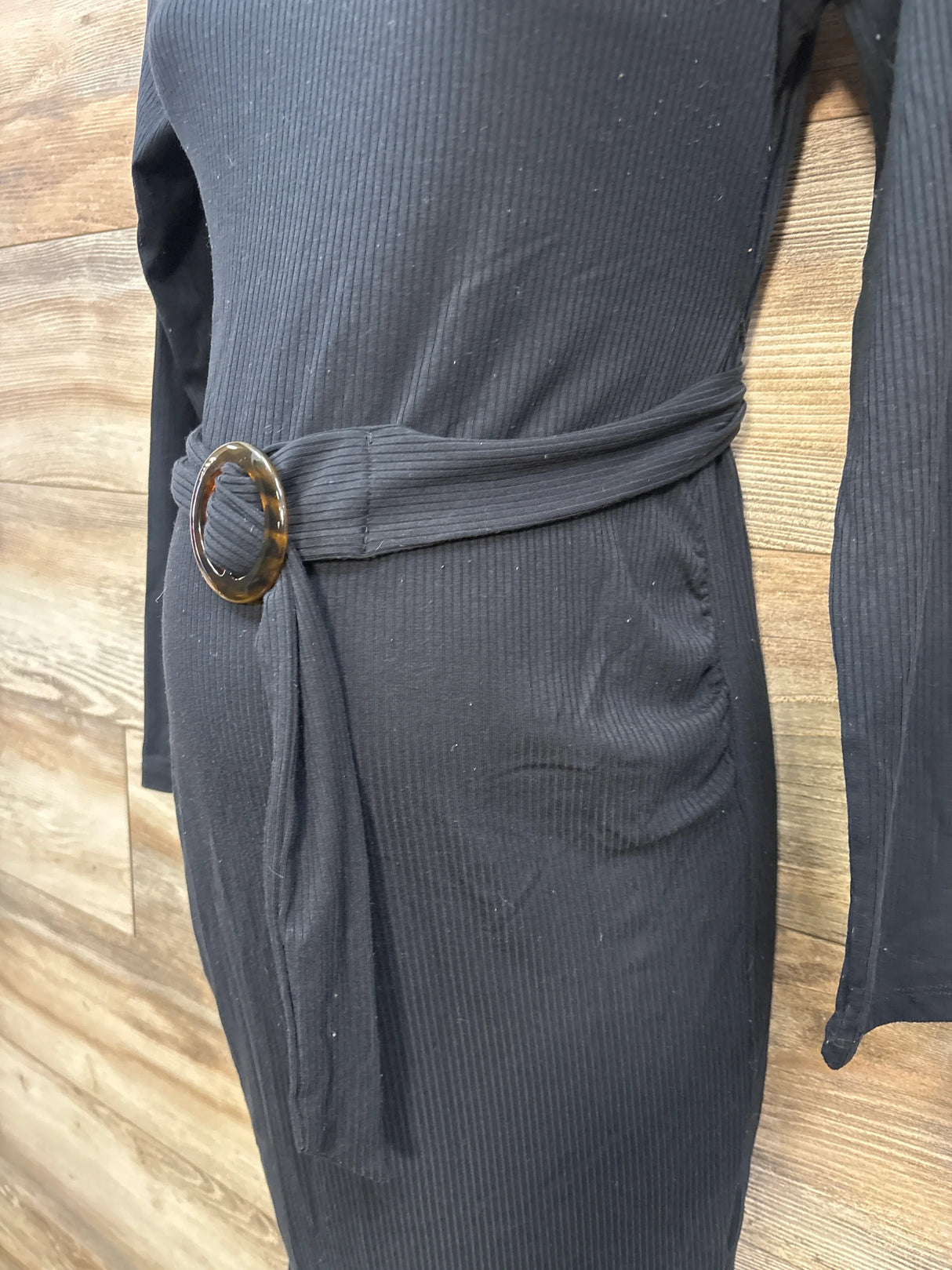 Black ribbed dress with tortoise shell belt buckle against wood wall background