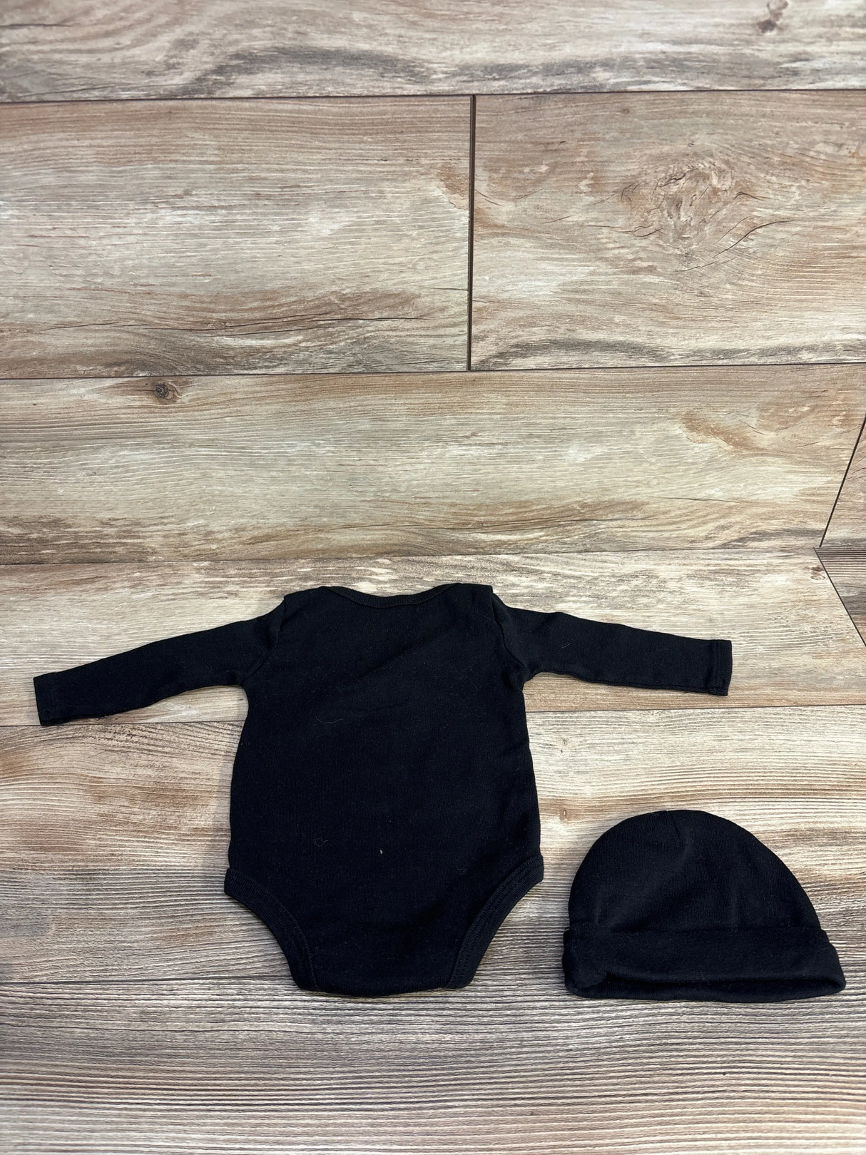Back view of Jordan two-piece set showcasing black long-sleeve bodysuit and matching beanie hat on wood plank floor