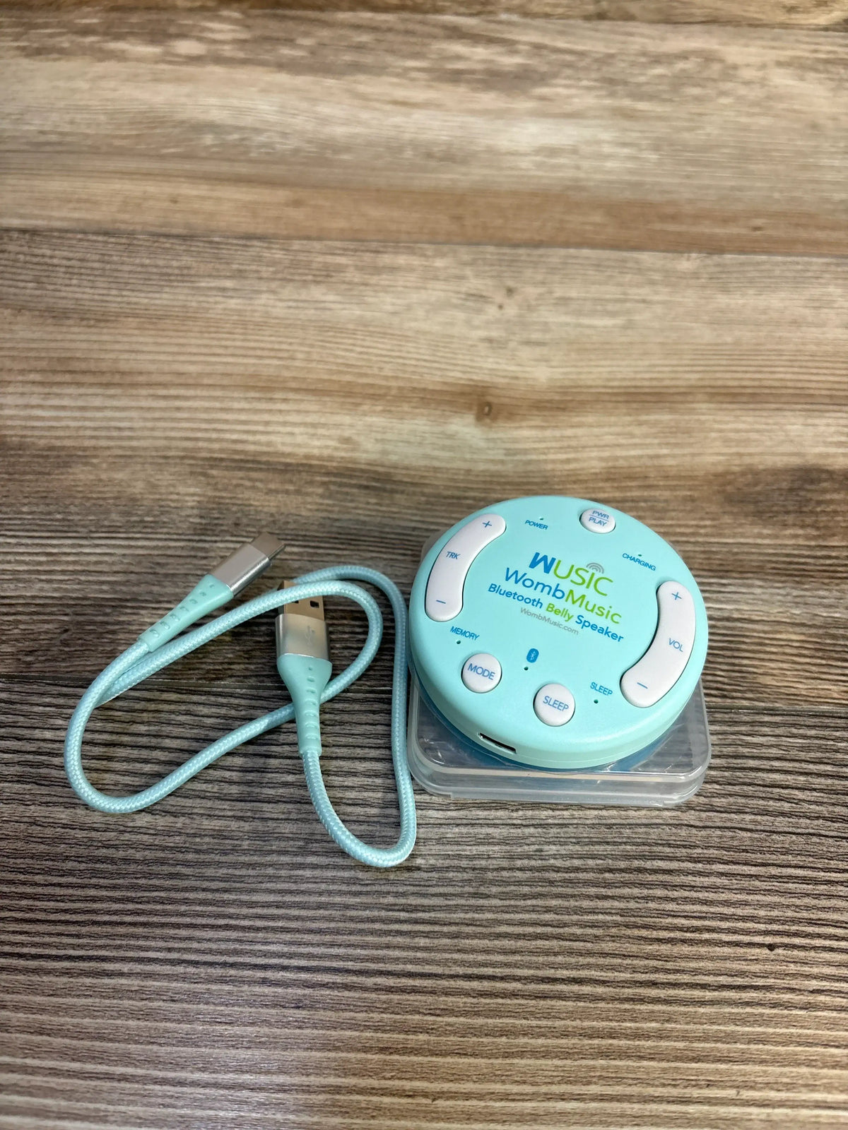 Womb Music Bluetooth belly speaker with USB charging cable on wooden surface