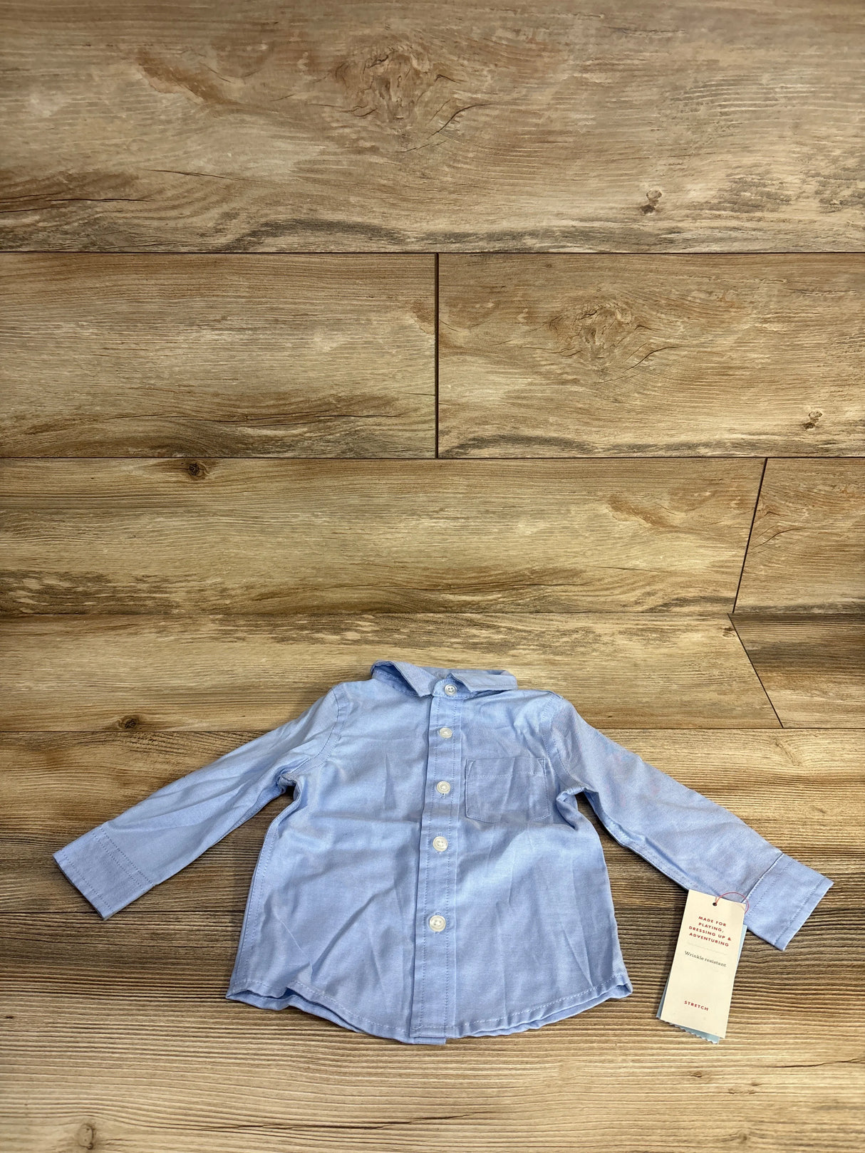 Light blue baby button-up shirt with collar on wood background and attached product tag
