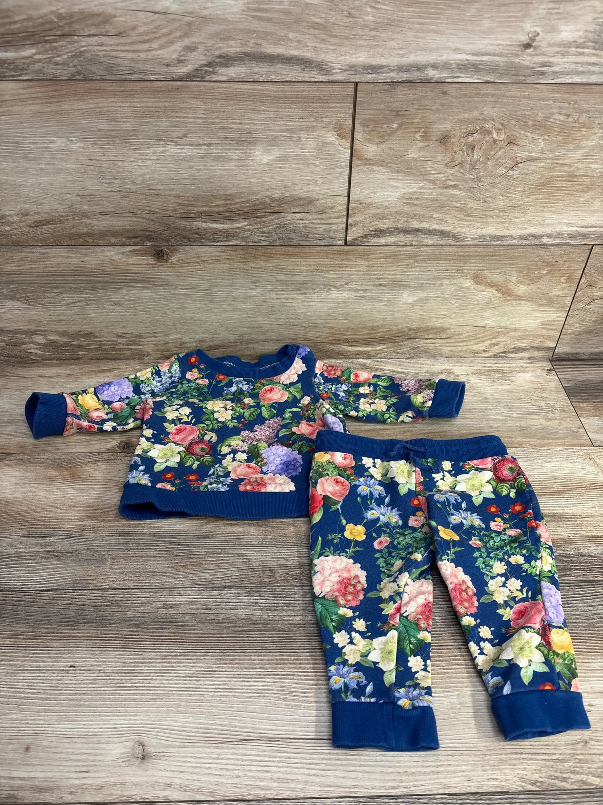 Floral print baby outfit with blue long sleeve top and matching pants on wood background