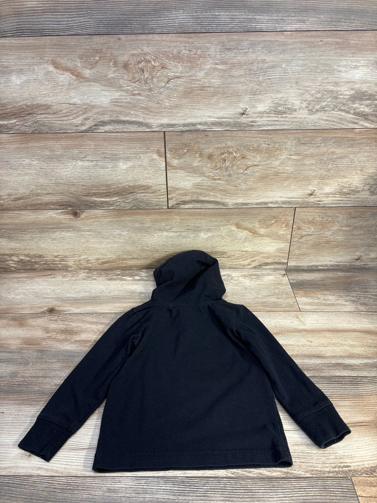 Back view of Nike hooded sweatshirt showcasing solid black knit with hood and cuffed sleeves on wood plank floor