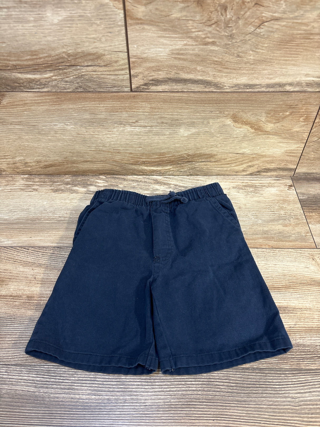 Navy blue kids shorts with elastic waistband, laid flat on wood floor