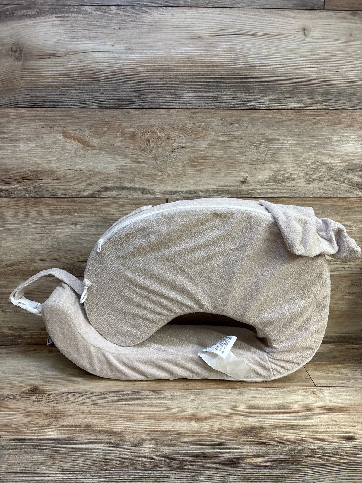 Top view of My Brest Friend Nursing Pillow in beige with a wraparound shape, strap, and zippered cover on wood