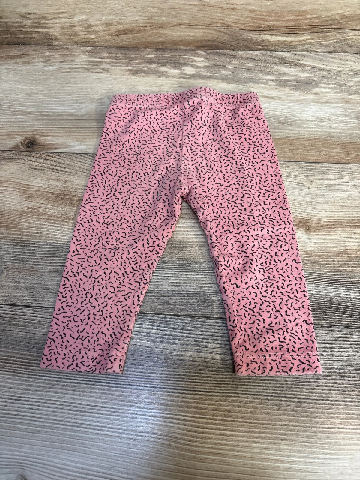 Pink baby leggings with black squiggle pattern on wood background