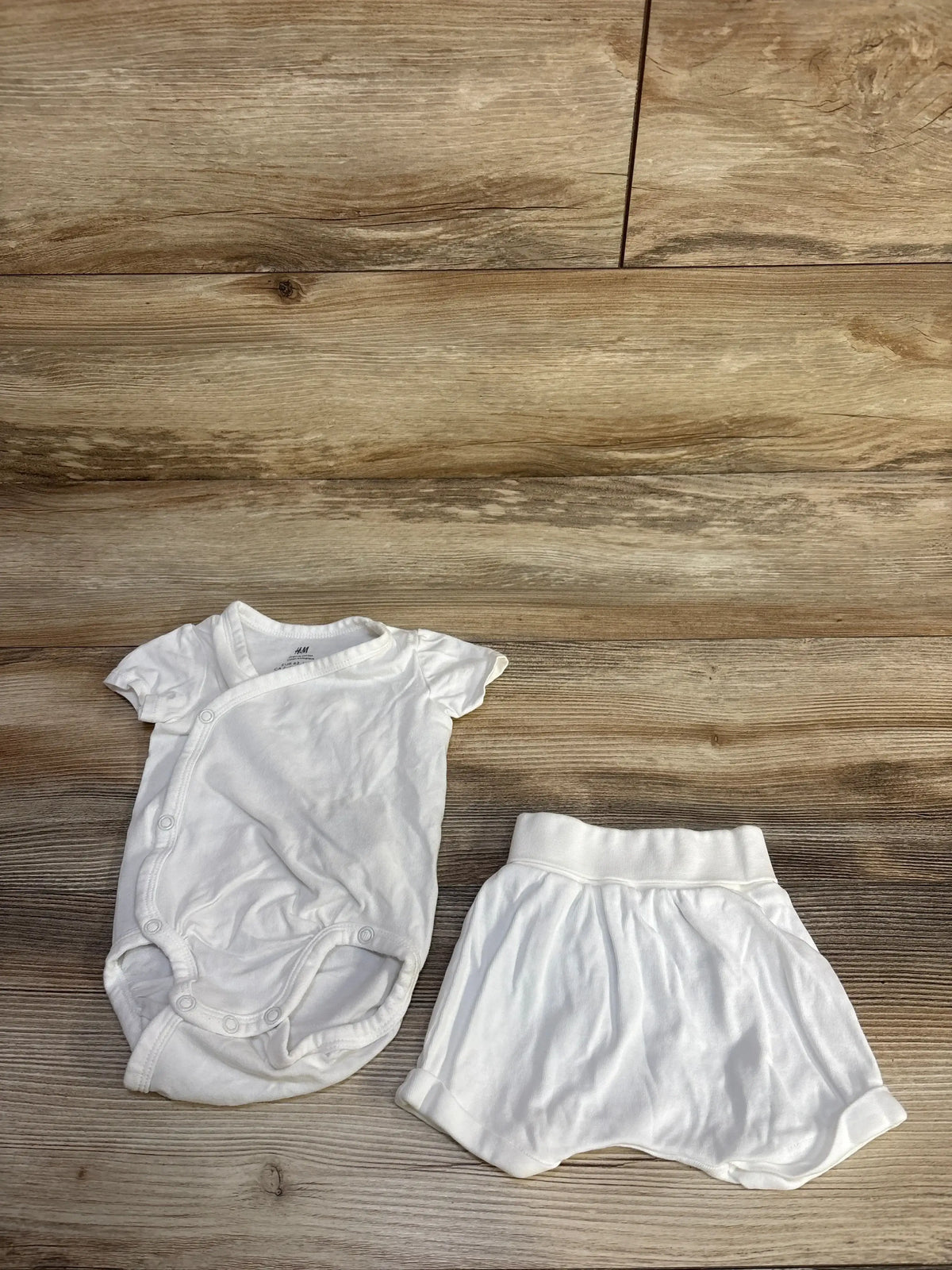 Flat lay of H&M white kimono bodysuit and foldover shorts showing side snaps and elastic waist on wood background