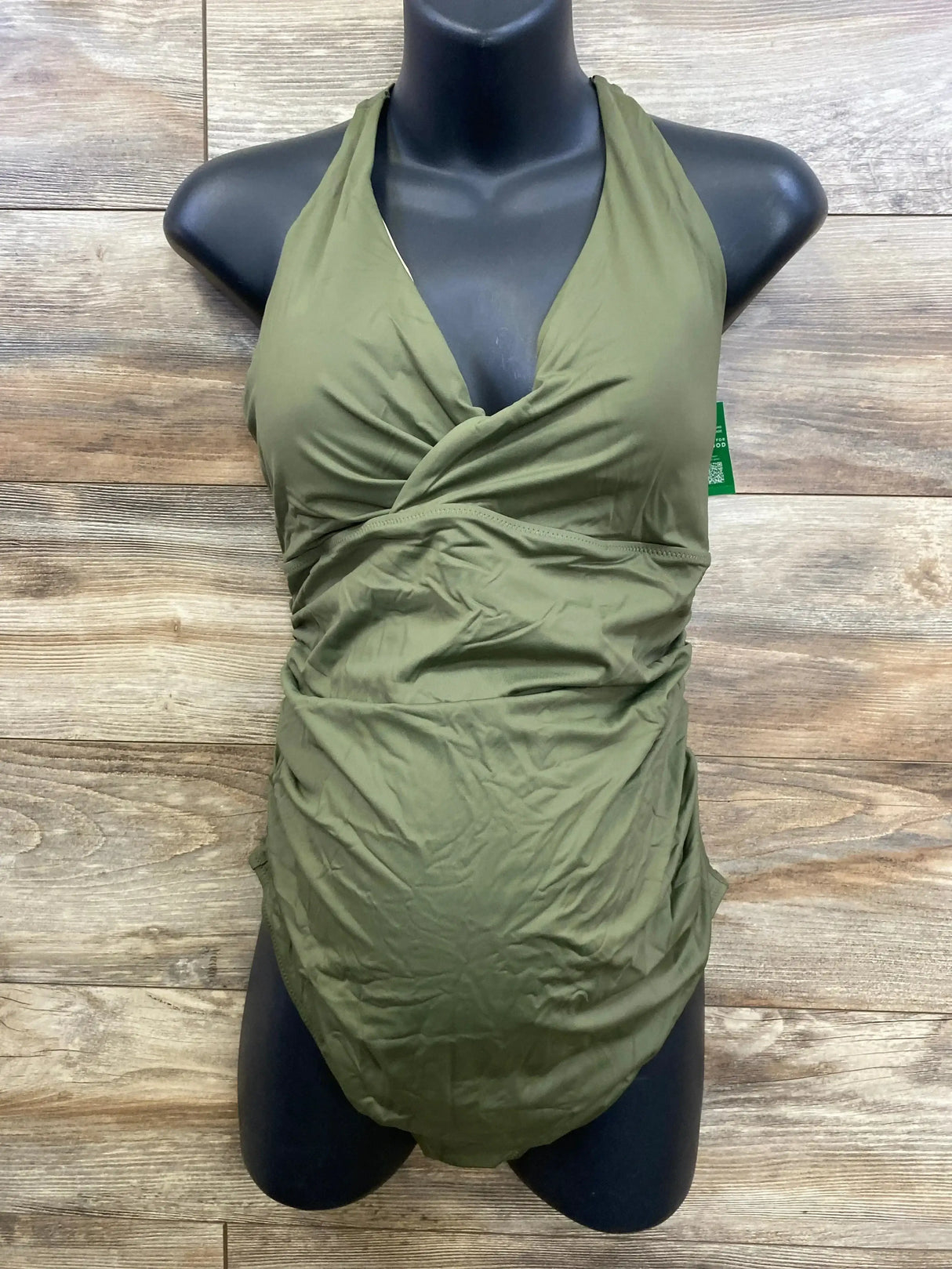 Front view of maternity one-piece wrap V-neck swimsuit in green with ruched sides on black mannequin against wood background