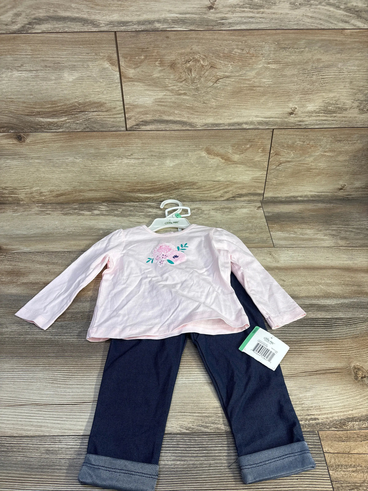 Front view of Little Me pink two-piece long sleeve shirt and jeggings set showcasing floral shirt graphic and cuffed pants on a wood floor