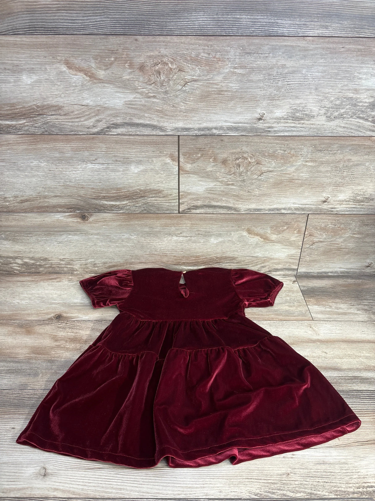 Burgundy velvet toddler dress with short puff sleeves on wood background
