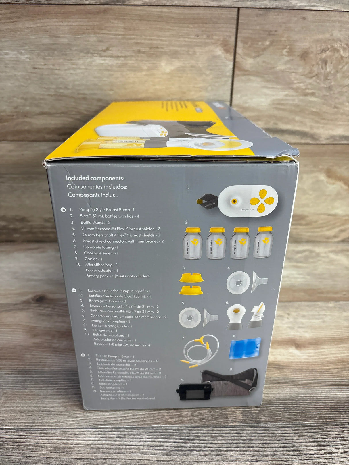 Side view of Medela Pump In Style with MaxFlow double electric breast pump yellow and grey box showing included components on wood plank floor