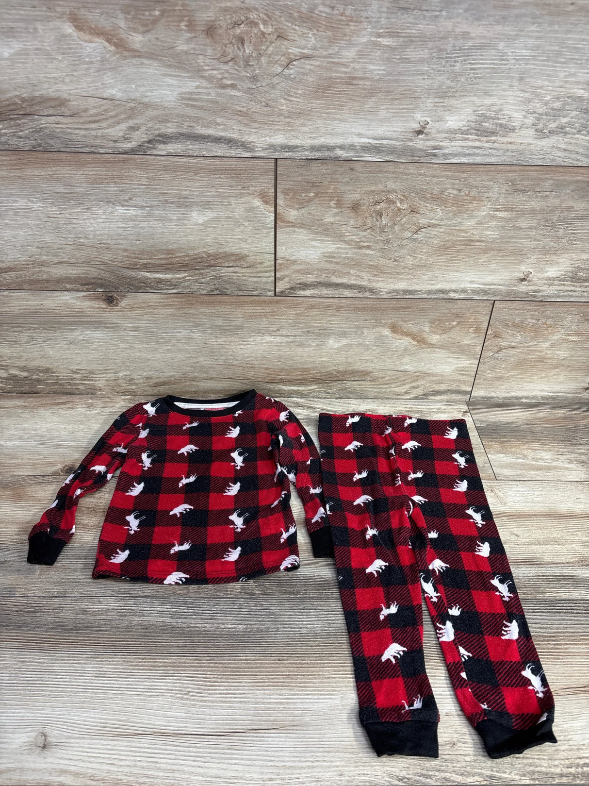 Flat lay of Dream Life 2pc red buffalo plaid pajama set 2T showing top and pants with white moose on wood floor
