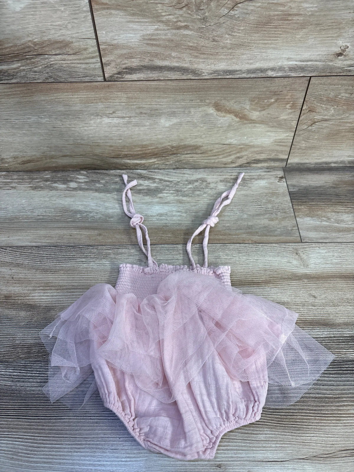 Front view of pink smocked tutu bubble romper showcasing layered tulle skirt and tie straps on a wood-grain floor