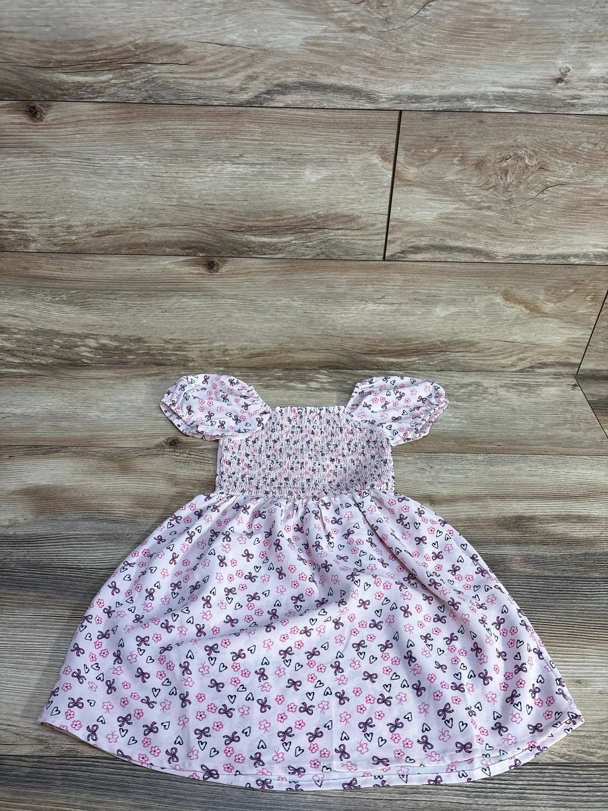 Front flat lay of pink smocked 2T dress with heart and bow floral print and puff sleeves on wood floor