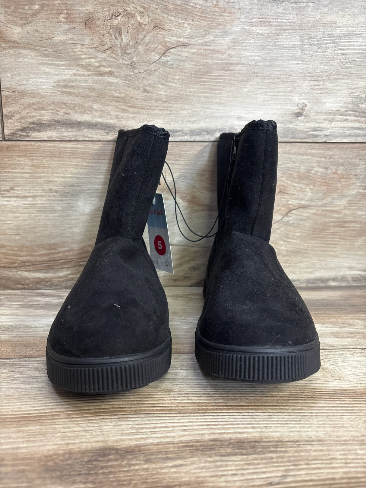 Pair of black kids' ankle boots with flat soles on wooden floor, size 5 tag visible