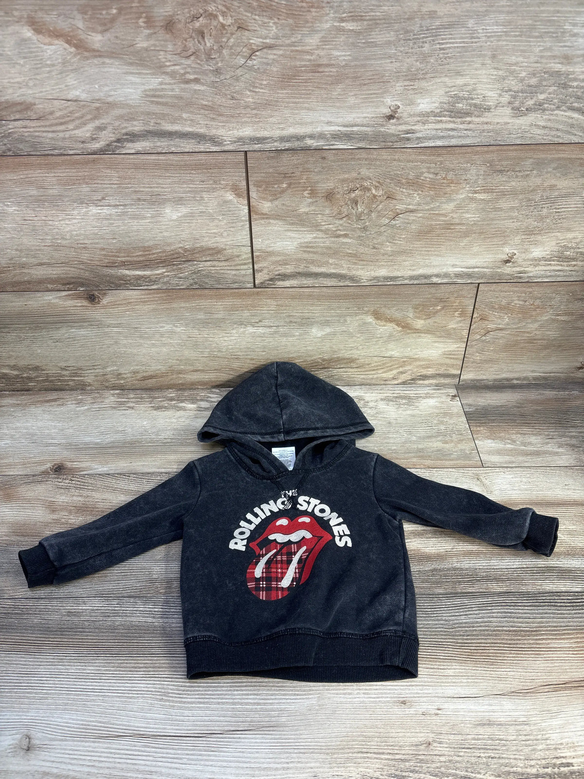 Front view of The Rolling Stones grey hooded sweatshirt for 12 months showcasing tongue graphic, hood, and front pocket on wood flooring