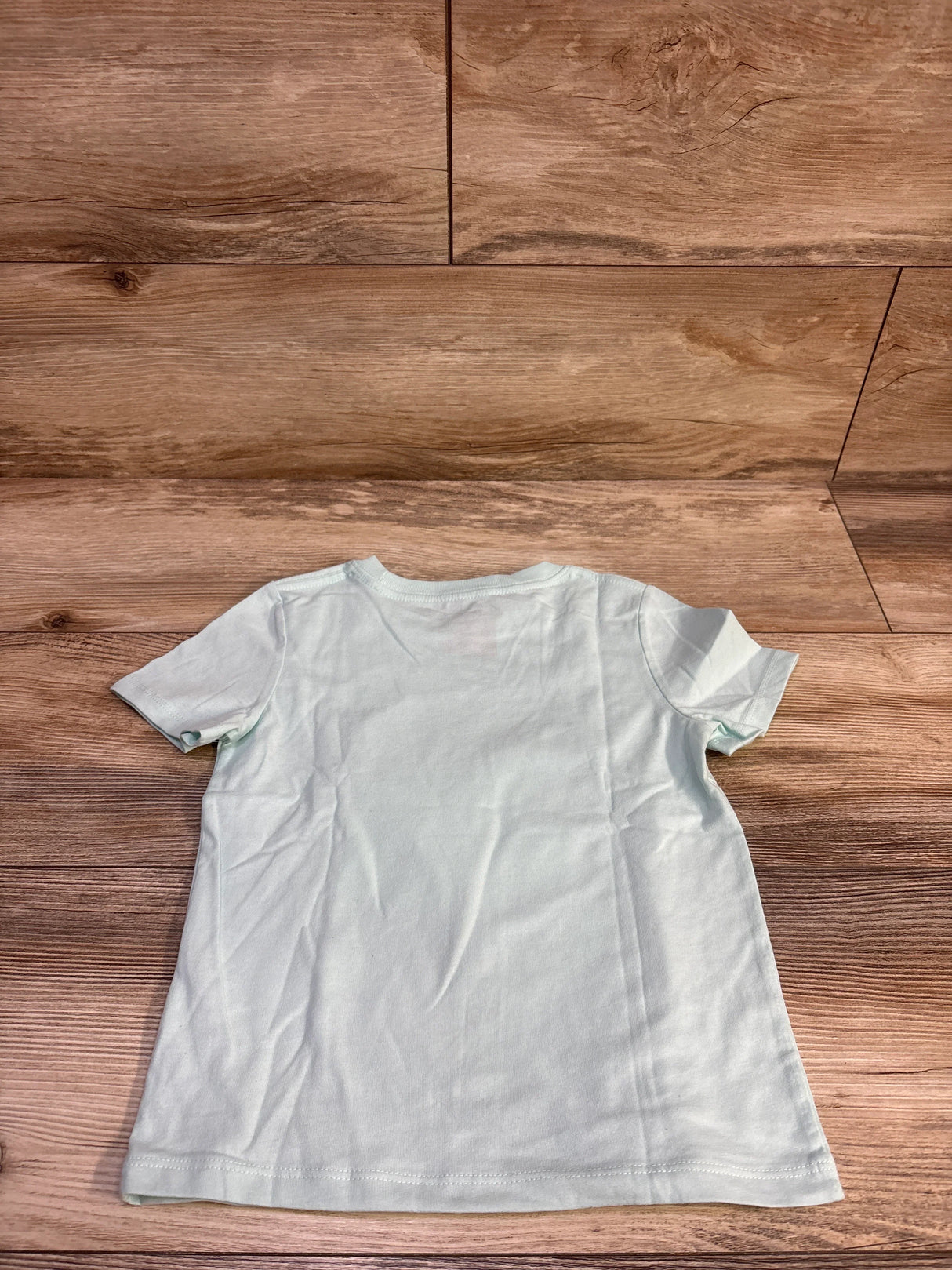 Back view of Cat and Jack toddler short-sleeve cloud shirt in light blue showing plain back on wood background, size 4T