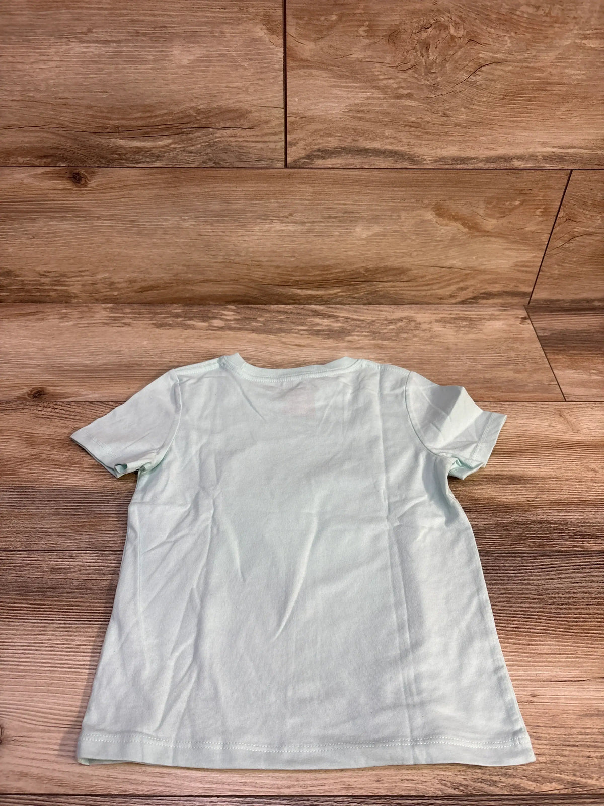Back view of Cat and Jack toddler short-sleeve cloud shirt in light blue showing plain back on wood background, size 4T