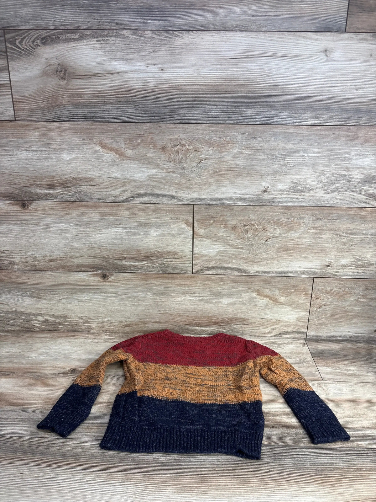 Kids knit sweater with red, mustard yellow, and navy blue color blocks, laid flat on wood floor