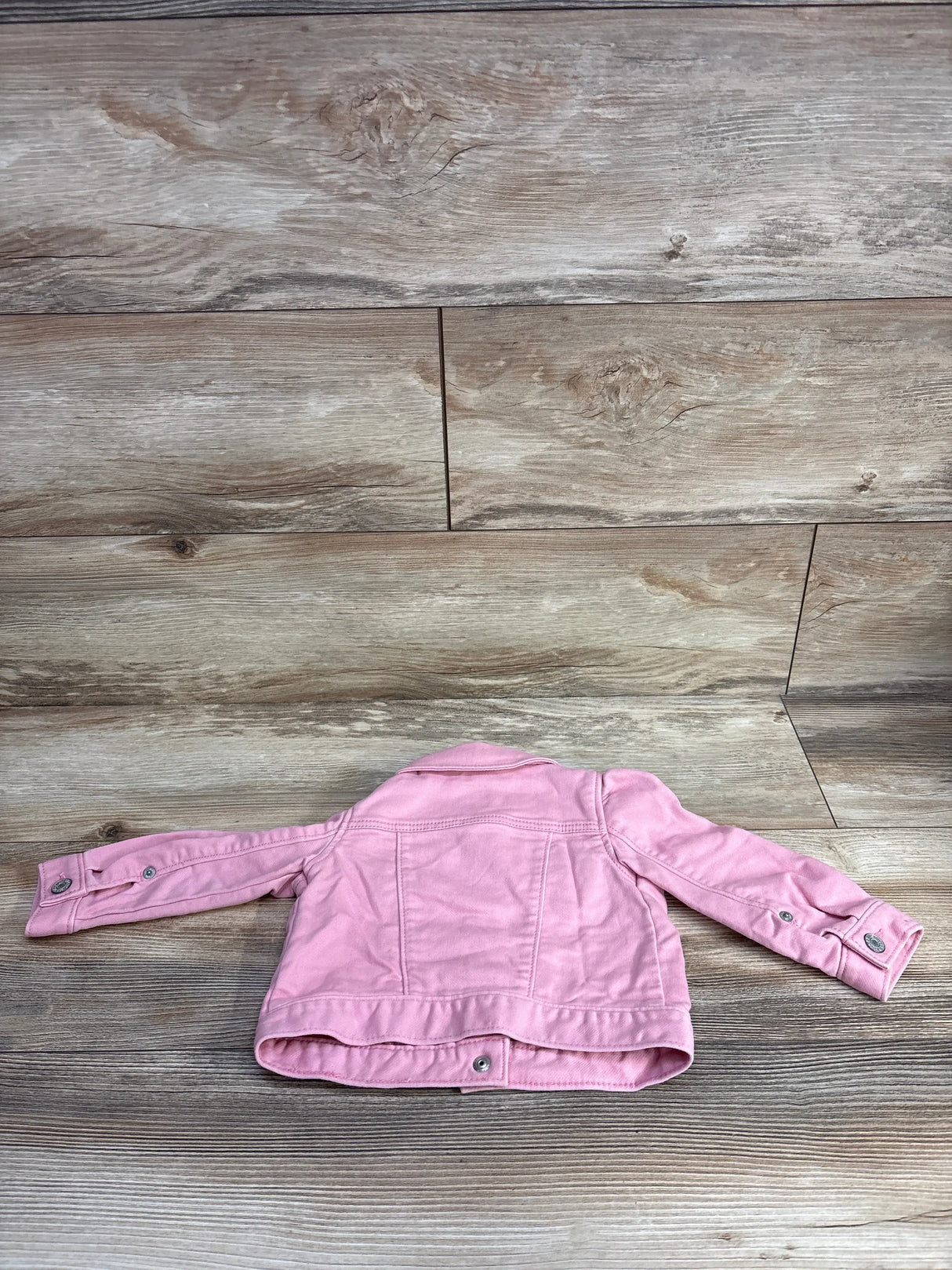 Back view of a pink toddler jacket laid flat on wood textured surface