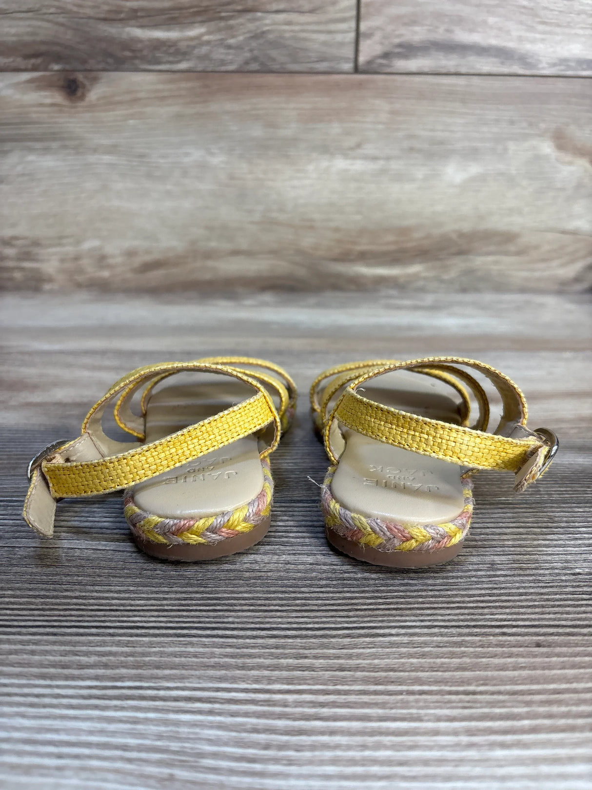 Back view of Janie & Jack Sunset Mood Straw Sandals size 6C showcasing yellow woven straps, braided straw trim, and ankle buckle on wooden floor