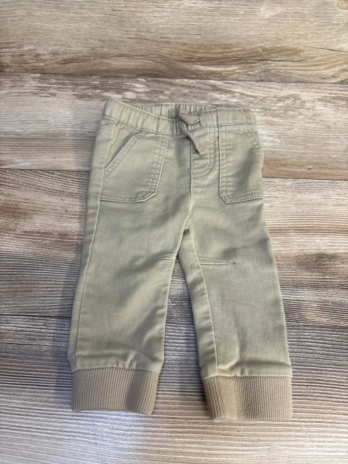 Beige toddler jogger pants with elastic waistband and cuffs on wood background