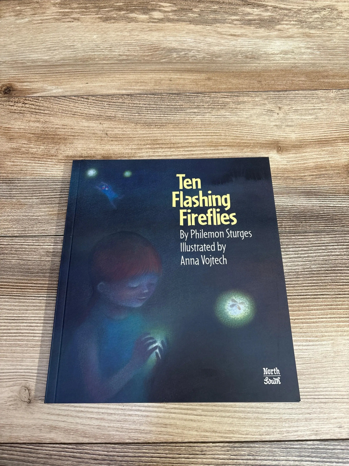 Children's book titled Ten Flashing Fireflies by Philemon Sturges and illustrated by Anna Vojtech on wooden table