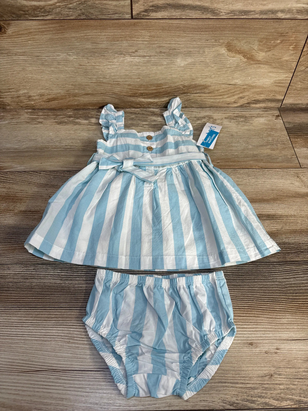 Top view of blue and white striped dress with matching bloomers, flutter sleeves, waist bow and wood buttons on wood floor