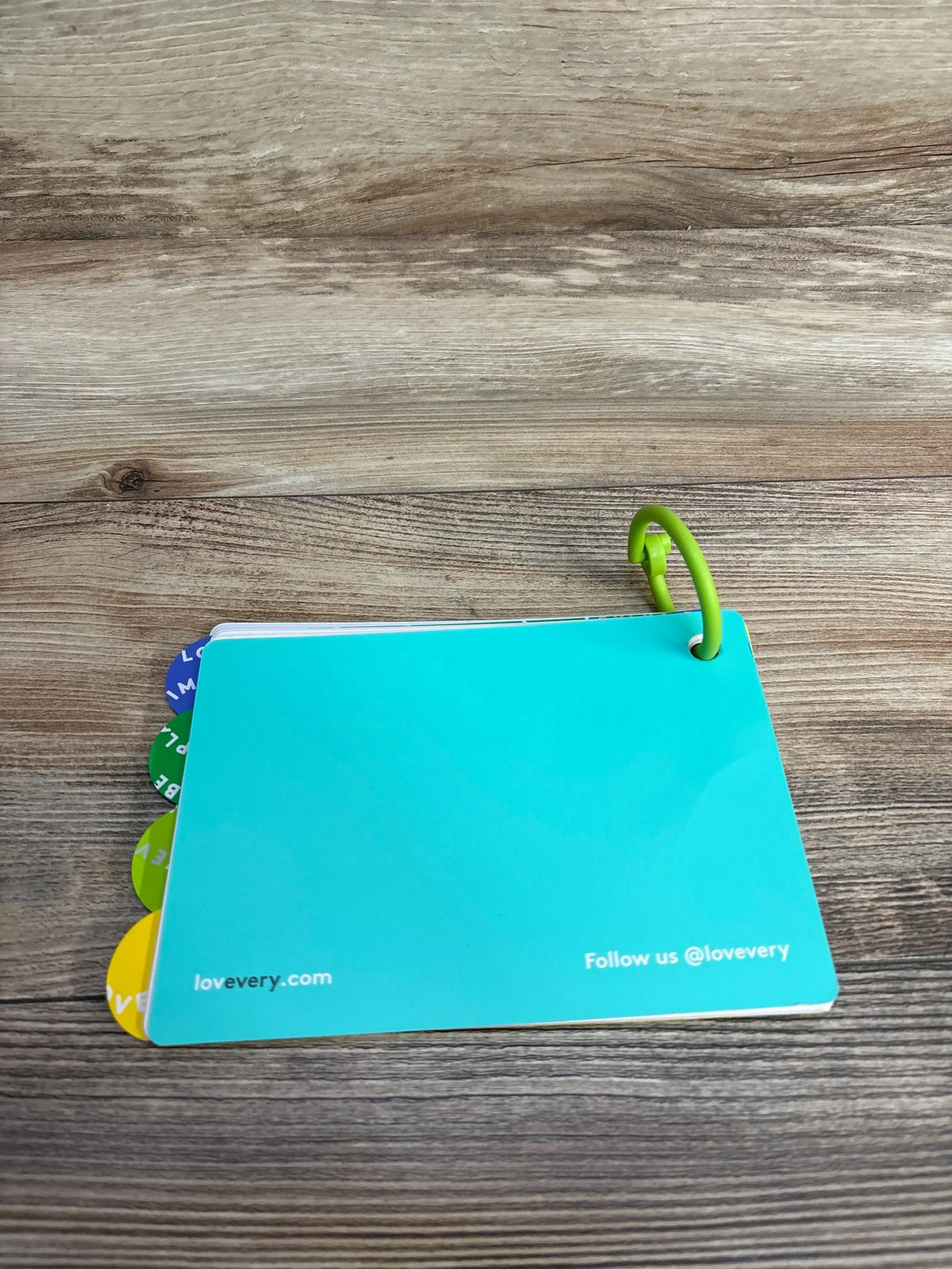 Top view of Lovevery Inspector play guide (7-8 months), mint cover with colorful tabbed cards and green ring on wood surface