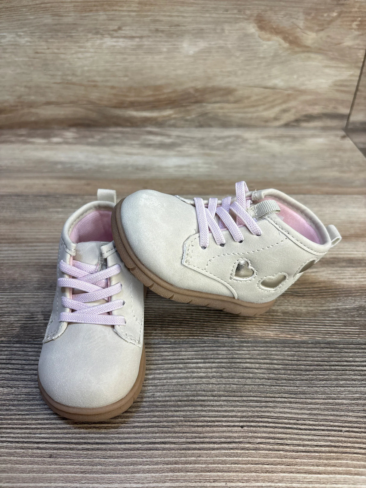 Angled view of Just One You Cressida first walker boots in tan with metallic heart cutouts, laces, lug soles, on wood