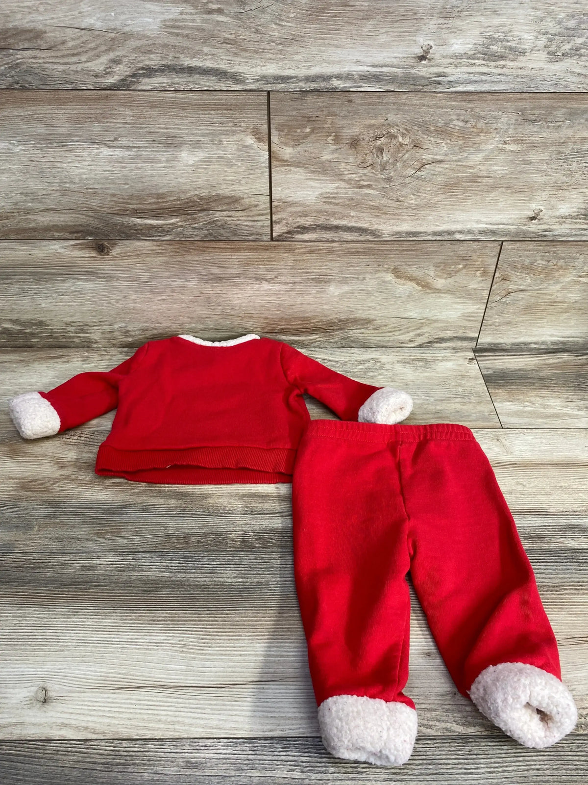 Red Santa-themed baby pajama set with white cuffs, laid on wood floor