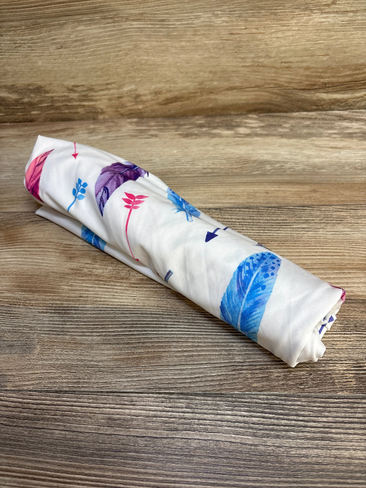Angled view of Gufix Multi-Use Cover (White Feathers) showcasing colorful feather and arrow print on a wooden surface