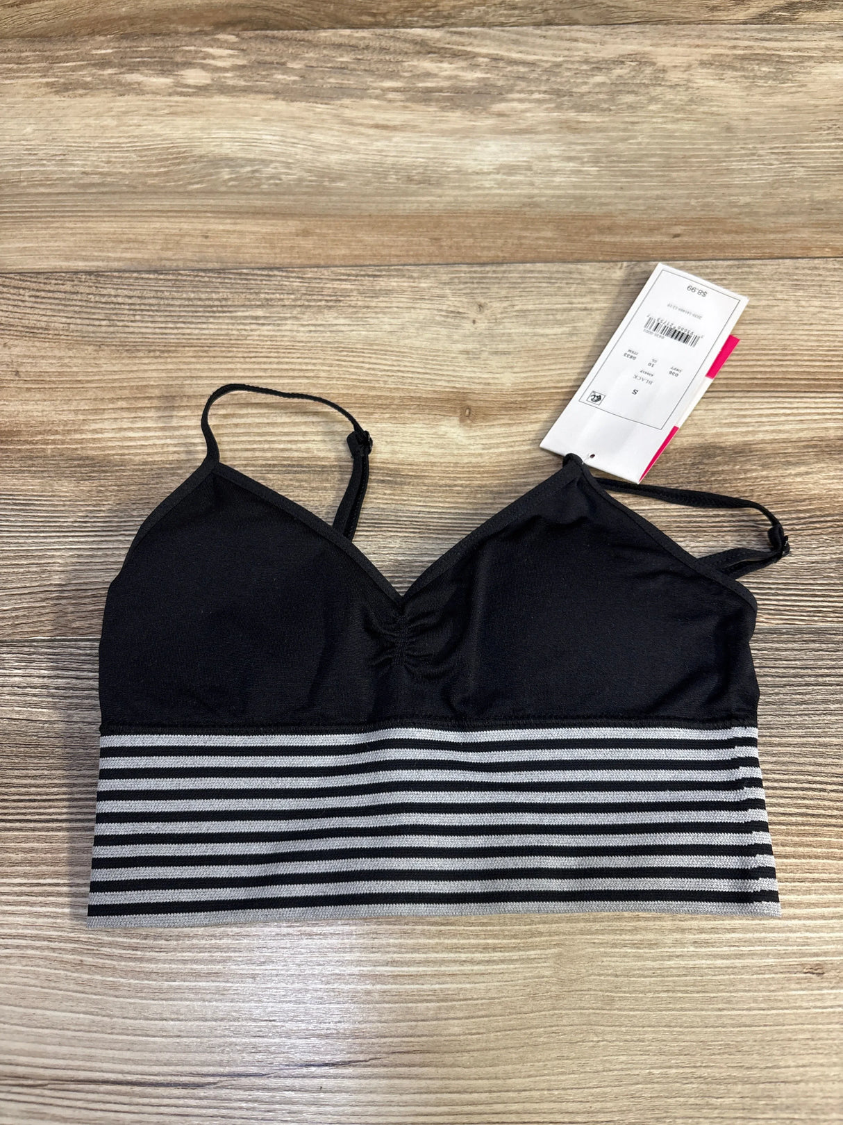 Black bralette with gray striped band and adjustable straps on wooden surface, retail tag attached
