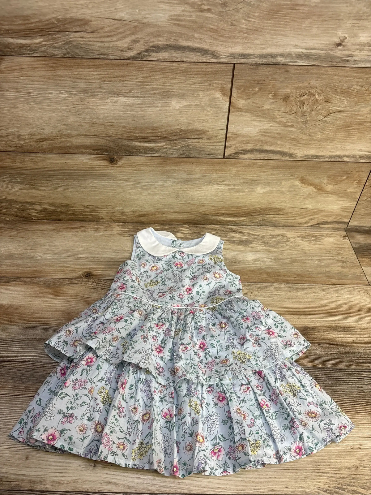 Flat lay of Janie and Jack light blue toddler floral dress with tiered ruffle skirt and white Peter Pan collar on wood floor