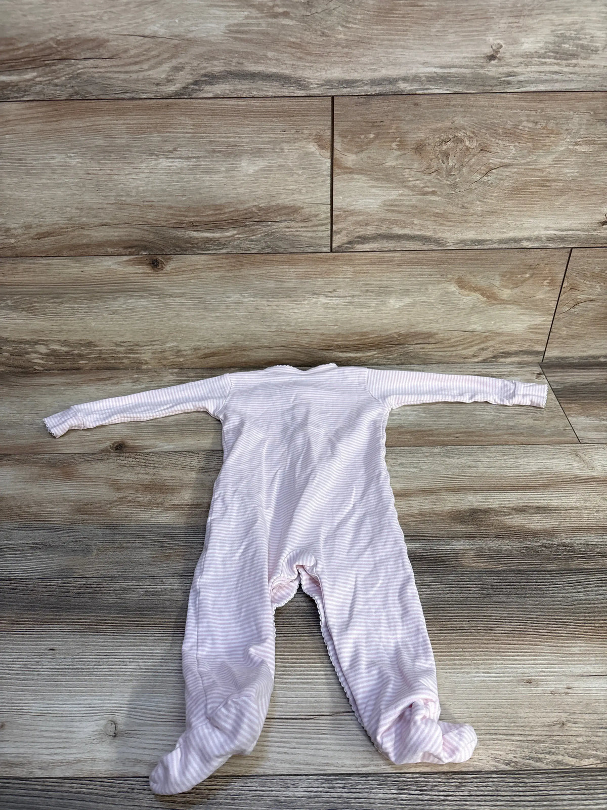 Flat lay of pink striped Kissy Kissy snap sleeper with long sleeves and footed legs on a wood-look background