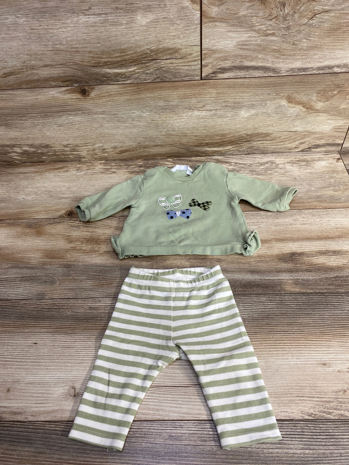 Children's outfit with light green bow-decorated top and white-green striped leggings on wooden floor