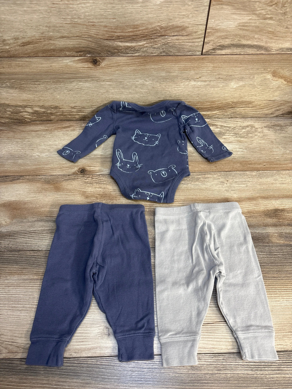 Baby onesie with animal print and two pairs of leggings, navy and gray, on wood floor