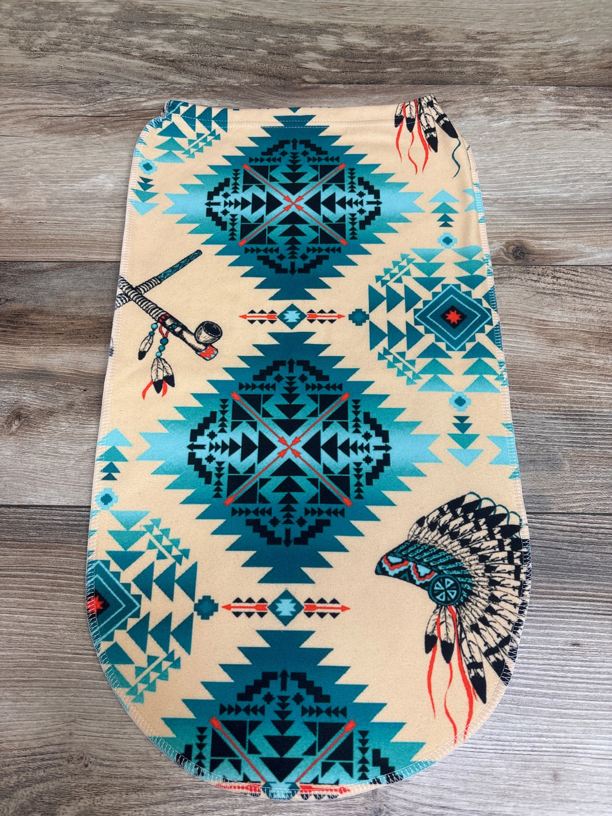 Front view of beige Native Design Swaddle Sack showcasing geometric and feather print with wood background