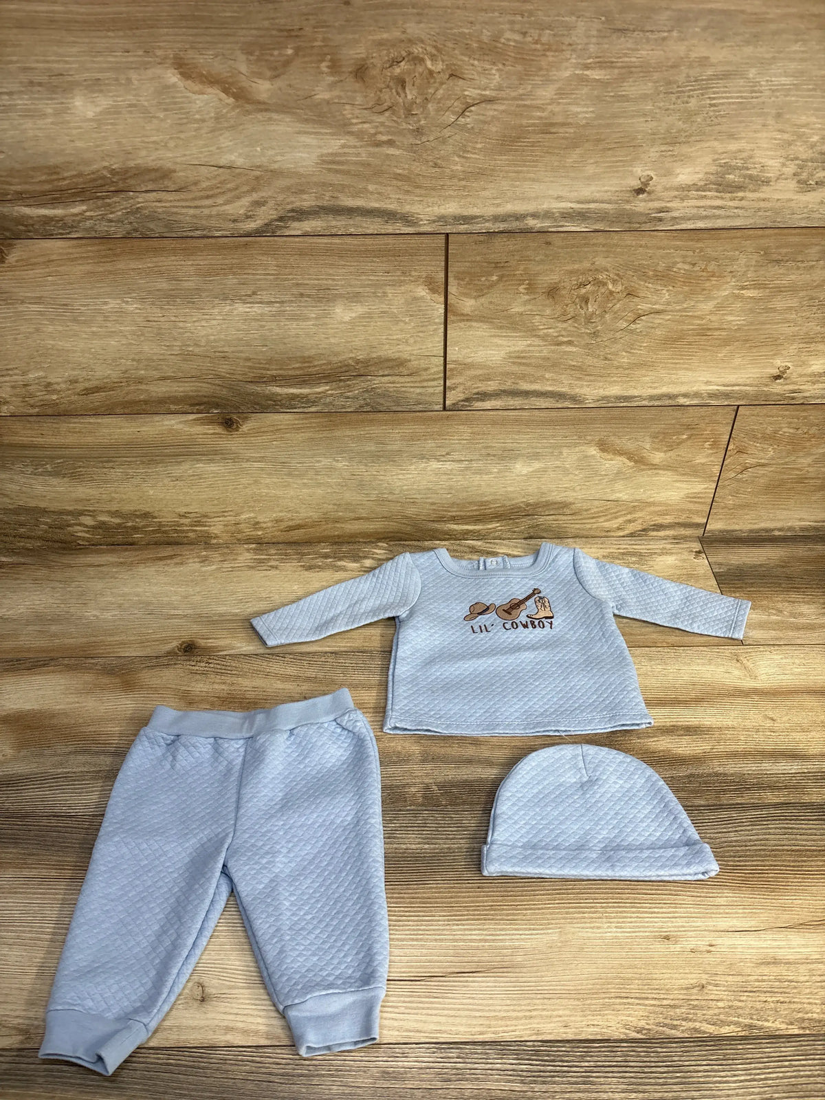 Front view of Sterling Baby 3-piece lil’ cowboy set showcasing blue quilted shirt, pants, and coordinating hat on wood
