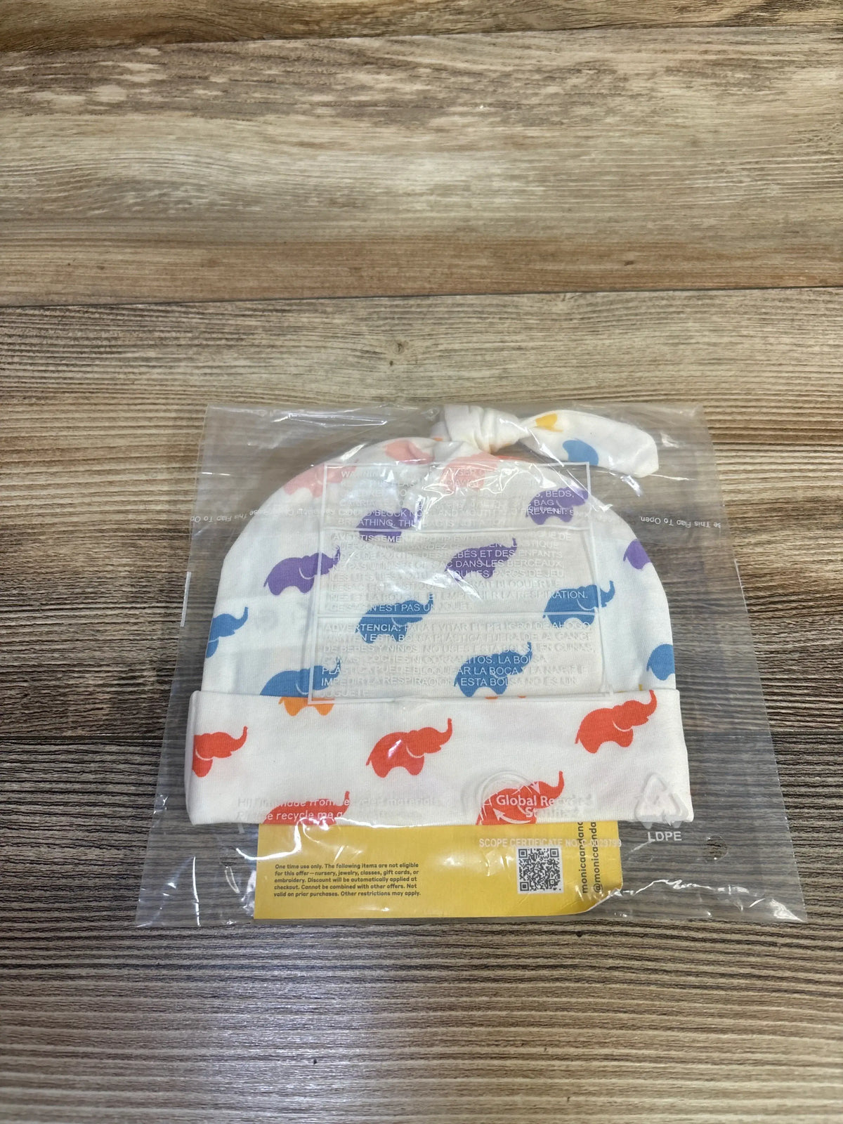 Front view of white elephant top knot cap showcasing multicolored elephant print in clear retail packaging