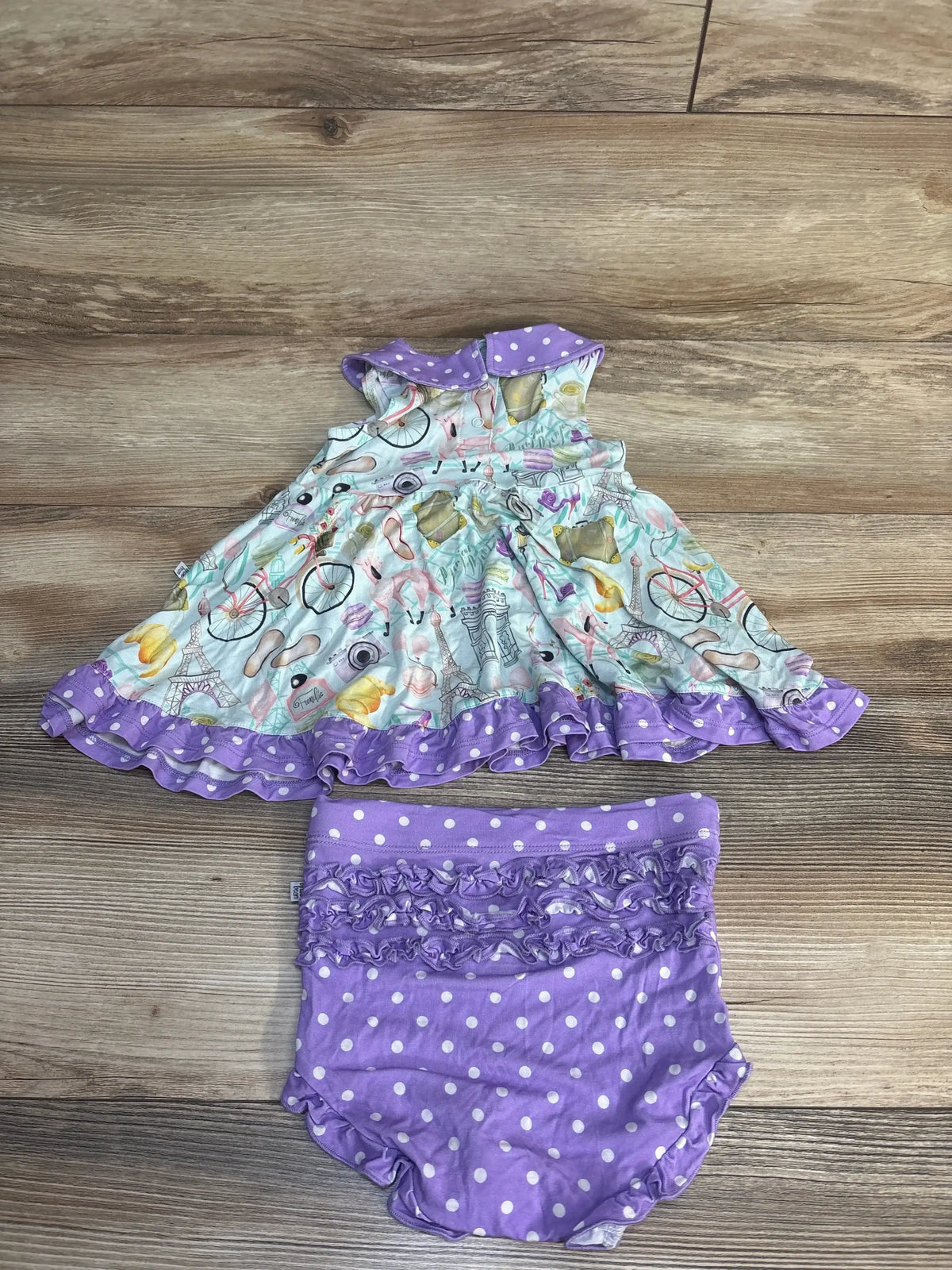 Top-down view of Birdie Bean Emilie Peplum Set sz 2T, printed top, Peter Pan collar, purple ruffle bummies on wood floor