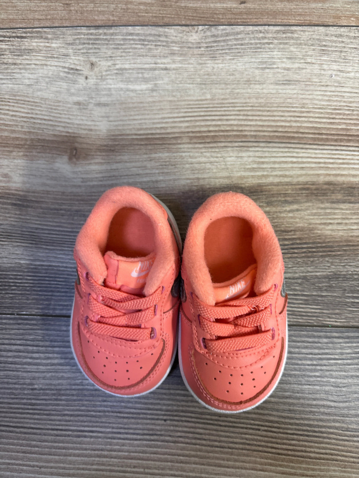 Top-down view of Nike Force 1 CB toddler sneakers showcasing atomic pink upper, metallic silver Swoosh, padded collar and white midsole on wood floor