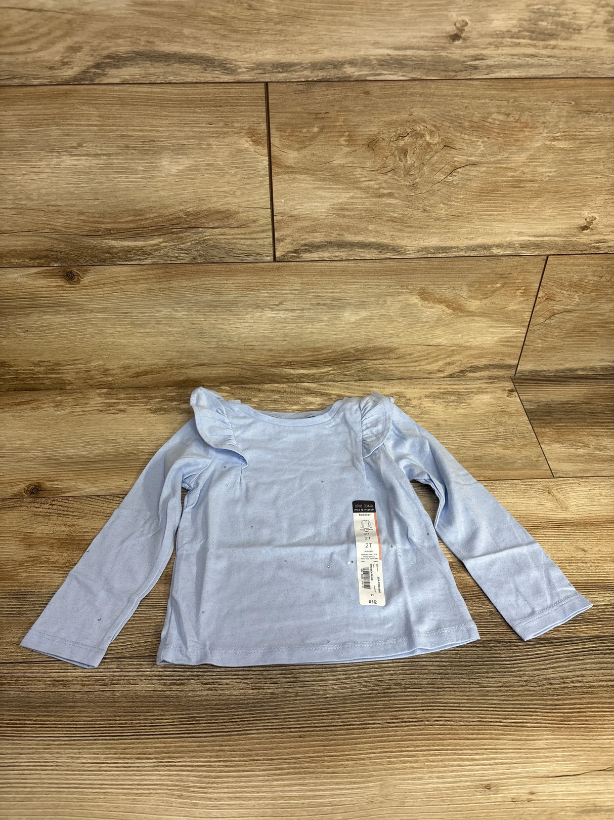 Light blue long sleeve toddler shirt with ruffle shoulders on wood background, resale kids clothing