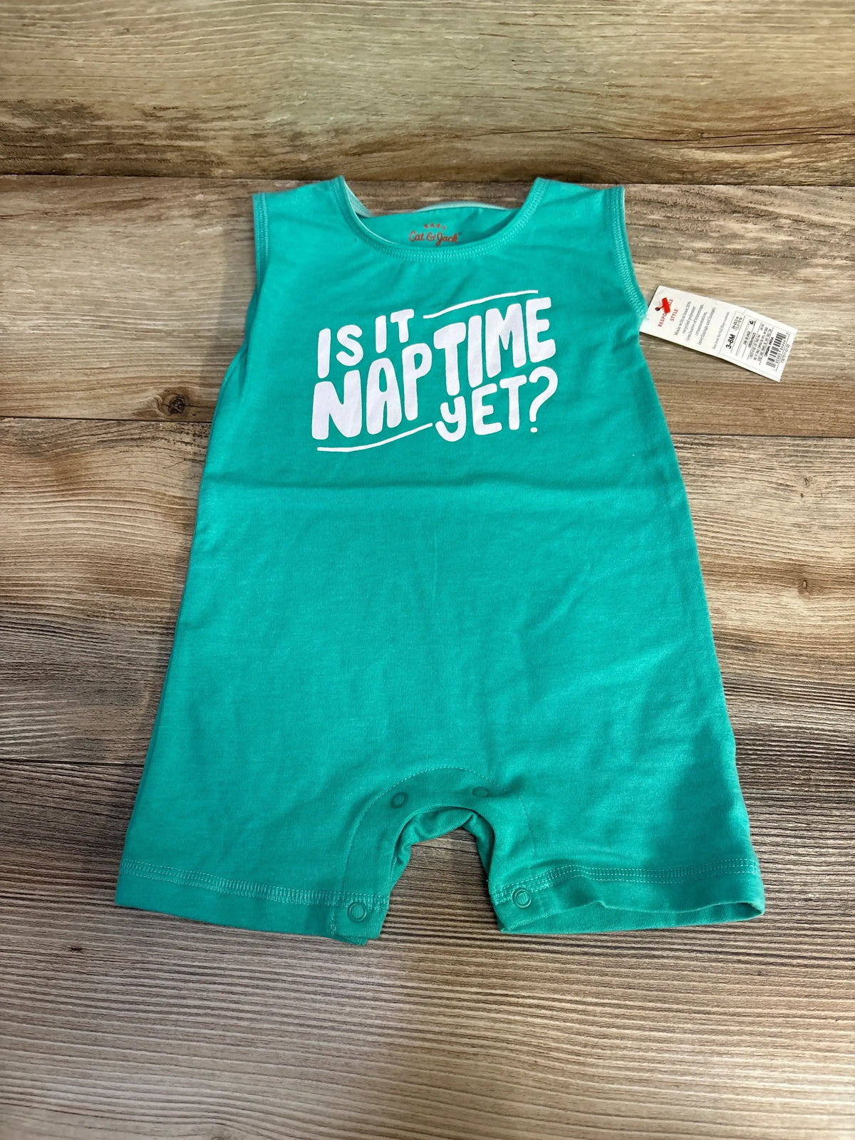 Flat-lay of green Cat & Jack sleeveless romper (3-6 months) with large white text ‘Is It Naptime Yet?’ on wood background