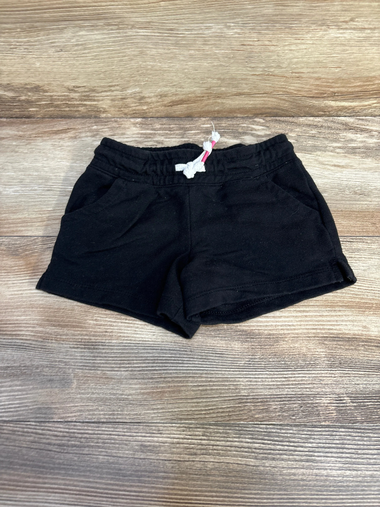 Flat-lay of black knit toddler shorts with elastic waistband, white drawstring, and front pockets on wood background