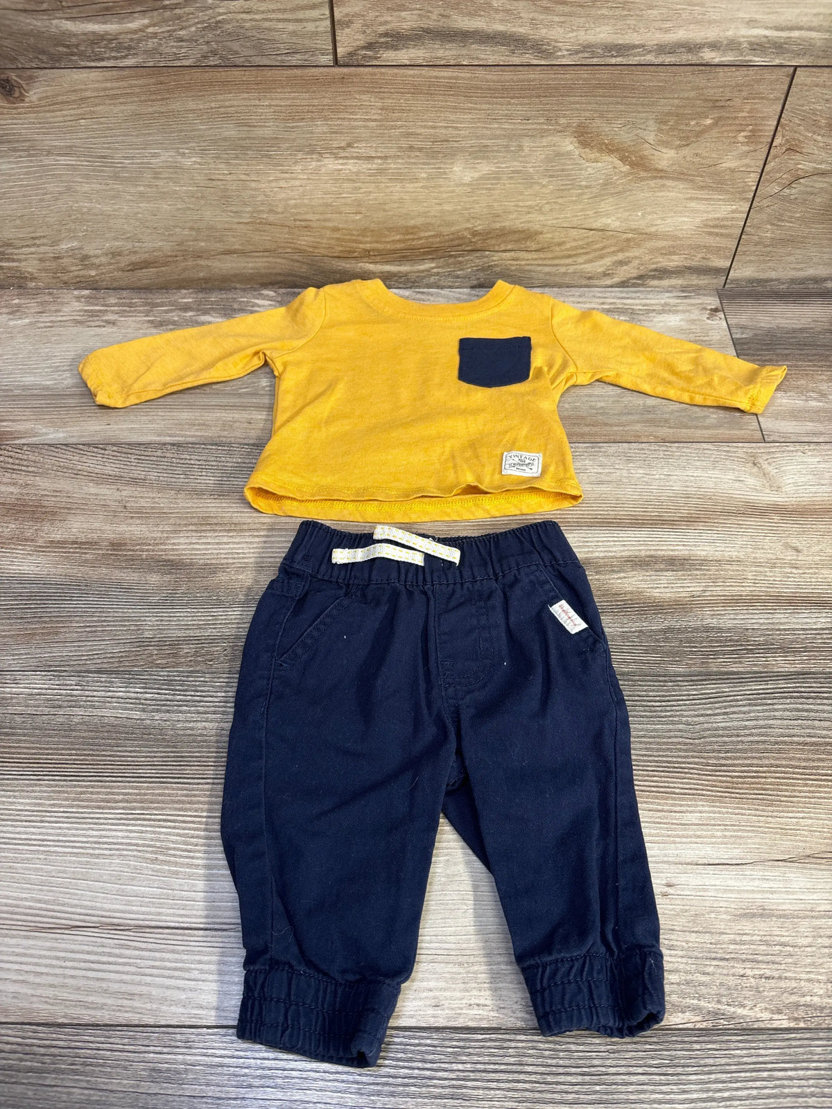 Top view of Weatherproof two-piece shirt and pants set with yellow long sleeves, navy pocket, and navy pants on wood floor
