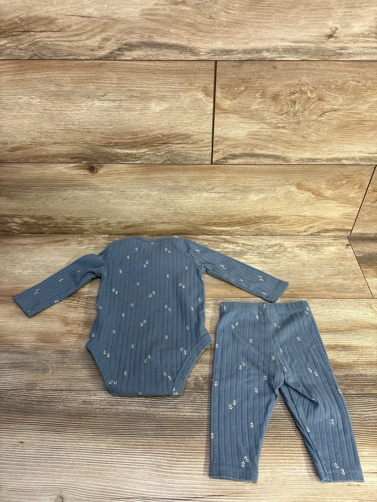 Flat lay of blue ribbed bodysuit and matching leggings with small white floral print on wood background