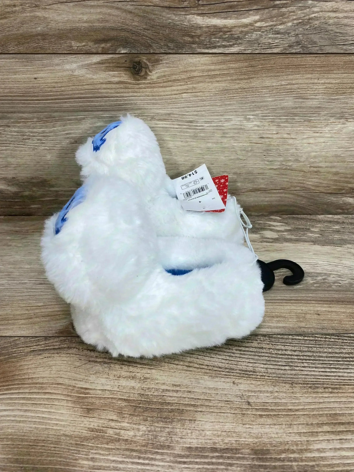 Side view of white plush Bumble slippers showcasing blue embroidered eyes and fluffy fur on wood background