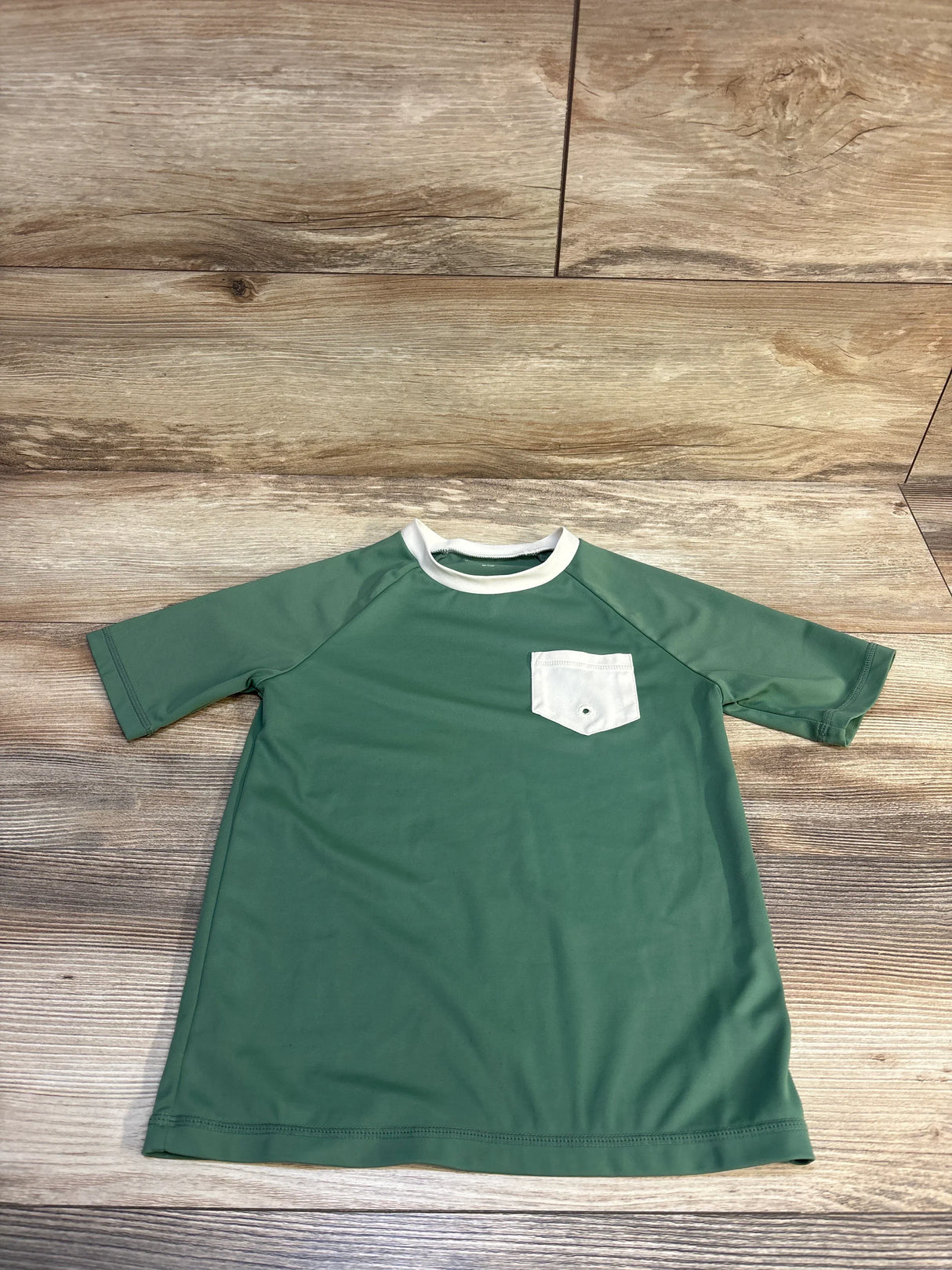 Green short sleeve kids shirt with white chest pocket on wood background