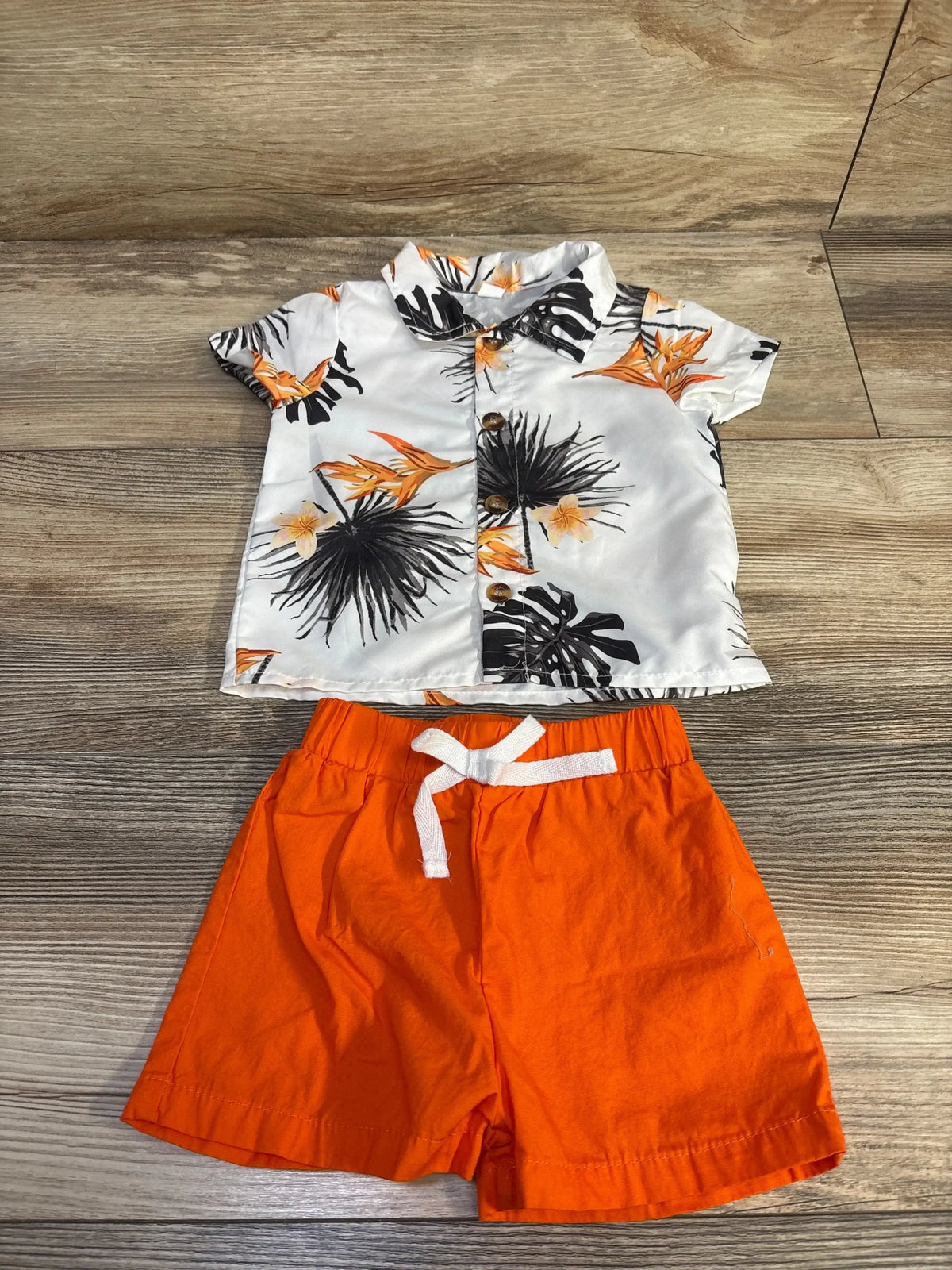 Flat lay of white button-up baby shirt with tropical print and wooden buttons, paired with orange drawstring shorts